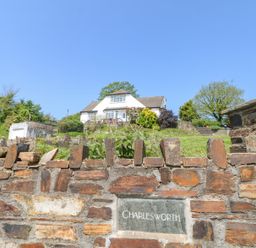 A brick wall with a nameplate reading Charlesworth and a white house with gardens behind it at Charlesworth in Braunton