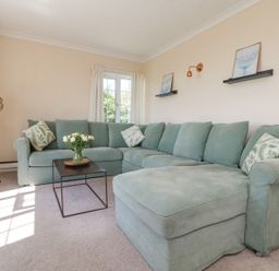 A living room with a green sectional sofa a black floor lamp and a small table with flowers at Charlesworth in Braunton