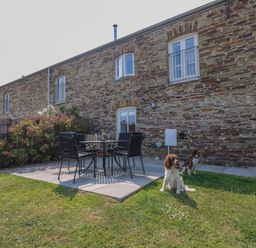 A stone building with a patio set and two dogs on grass at Sundowner in Padstow