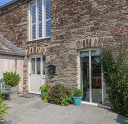 Stone house exterior with white door and window and potted plants on patio at Sundowner in Padstow