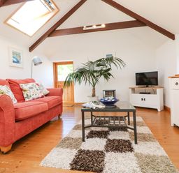A living room with a red sofa a glass coffee table a patterned rug a potted plant a television and wooden beams on the ceiling at Lower Rissick Cottage in Sennen