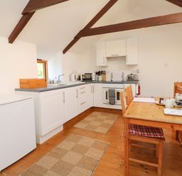 A kitchen with white cabinets wooden dining table with chairs and wooden beams on ceiling at Lower Rissick Cottage in Sennen