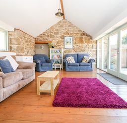 A living room with sofas a coffee table a purple rug and a bookshelf at The Old Barn in Sennen