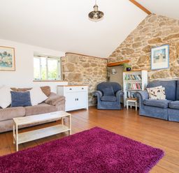 A living room with a brown sofa a blue armchair a blue couch a white cabinet a bookshelf and a purple rug at The Old Barn in Sennen