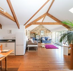 An open living space with wooden beams a kitchen area wooden floor and seating at The Old Barn in Sennen