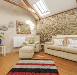 A living room with beige sofa and armchair a striped rug and a side table with flowers at Barneys Barn in Sennen