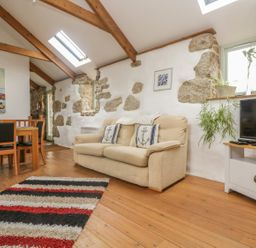 A living room with a beige sofa and dining table with chairs on wooden floor at Barneys Barn in Sennen