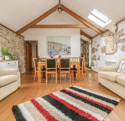 A living room with wooden floor beams stone walls a dining table with chairs and sofas at Barneys Barn in Sennen