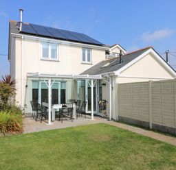 A backyard with a white patio set on a paved area next to a beige house with solar panels on the roof at Ridgeback House in Mullion