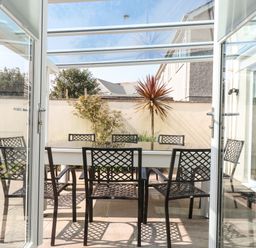 A patio dining area with a table and six black lattice chairs under a glass roof at Ridgeback House Mullion