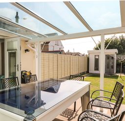 An outdoor covered patio with a table and chairs overlooking a fenced garden with a shed and a clothesline at Ridgeback House in Mullion