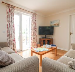 A living room with two beige sofas a wooden coffee table a television on a wooden cabinet and floral curtains at Tre Pol Pen in Falmouth