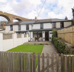 A fenced backyard with a lawn dining chairs and stone path behind a terraced house with a viaduct in the background at Anneth Lowen in Angarrack near Hayle