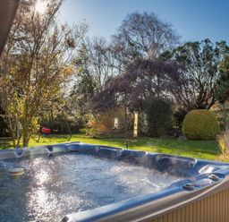 A bubbling hot tub in a garden with trees shrubs and a children's swing set at Nairn in Braunton