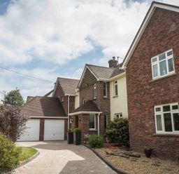 A driveway leading to a two garage doors attached to a brick and cream house with plants in pots at Nairn in Braunton