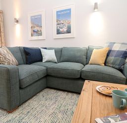 A living room with a sectional sofa with cushions a wooden table with two mugs and pastries at Hazel Barn in Falmouth