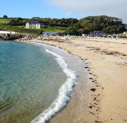 A sandy beach with small waves meeting the shore and houses on green hills at Hazel Barn in Falmouth