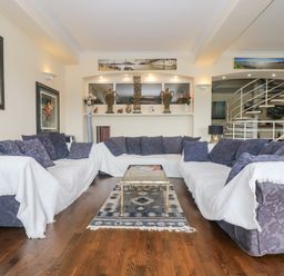 A living room with three sofas covered with white throws and a glass coffee table on a patterned rug at Bight Boathouse in Dartmouth