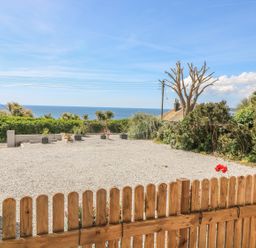 A fenced gravel yard with plants and a view of the sea at Hagar Vor in Marazion
