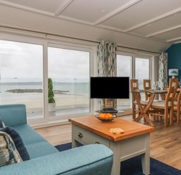 A living room with a blue sofa and wooden coffee table next to large windows overlooking the beach at Higher Mount View in Marazion