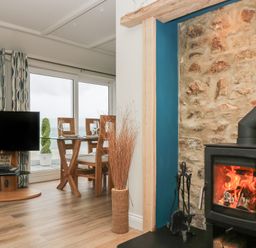 A living area with a wood stove fireplace a glass dining table with chairs a television and large windows at Higher Mount View in Marazion