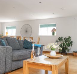 A living room with a gray sofa wooden coffee table with flowers and a bottle at Lake View in Kingsand and Cawsand