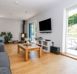 A living room with a wood stove a television on the wall a coffee table and sliding glass doors at Lake View in Kingsand and Cawsand