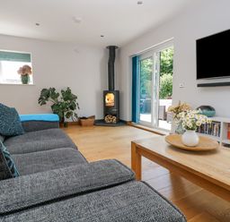 A living room with a gray sofa a wooden coffee table flowers a stove and a wall mounted television at Lake View in Kingsand and Cawsand