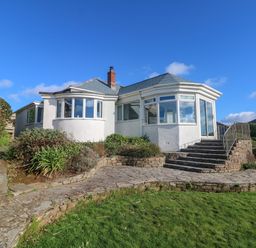 A white house with large windows stone steps and a stone path surrounded by grass and shrubs at Gwillen in Mawgan Porth