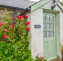 A garden entrance with red roses and green door at Goslings in Bradford Holsworthy