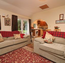 A living room with two sofas and a red patterned rug with an open kitchen visible through an arch at Goslings Bradford Holsworthy
