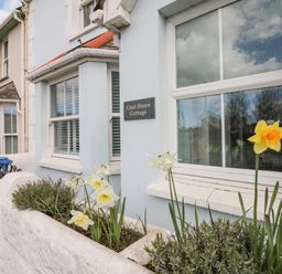 The exterior of a light blue cottage with a flower bed in front of the windows at Cool Stone Cottage Instow near Bideford