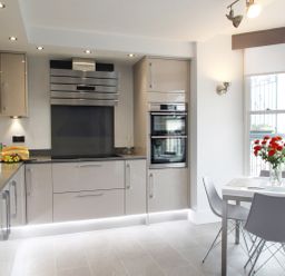 A kitchen with beige cabinets a stovetop oven and a dining table with chairs and flowers at 5 Arlington Villas in Ilfracombe