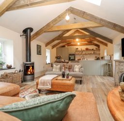 A living room with exposed wooden beams a fireplace leather sofas and a kitchen area at Trevoole Barn in Praze An Beeble