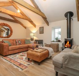 A living room with sofas a fireplace and wooden beams at Trevoole Barn in Praze An Beeble