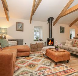 A living room with sofas a wood burning stove and a patterned rug at Trevoole Barn in Praze An Beeble