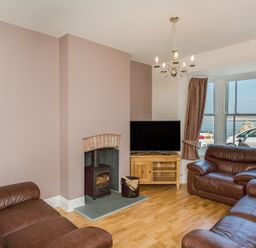A living room with leather sofas a wood stove a television on a wooden stand and a window showing parked cars and water at The Crab Shell in Appledore near Bideford