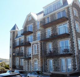 A stone building with multiple balconies and parked cars in front at Ocean Breeze in Ilfracombe