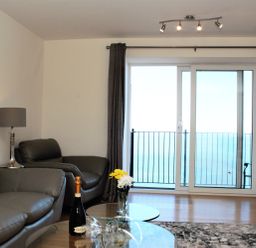 A living room with leather sofas a glass coffee table with a bottle and glasses and a balcony door showing the sea at Ocean Breeze in Ilfracombe
