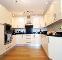 A kitchen with beige cabinets black countertops wooden floor and appliances at Ocean Breeze in Ilfracombe