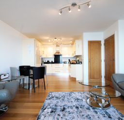 An open-plan living room and kitchen with grey leather chairs glass dining table and wooden floor at Ocean Breeze in Ilfracombe