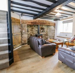 A living room with two leather sofas a coffee table a rocking chair a stone fireplace and stairs at Tai Ucha in Cerrigydrudion