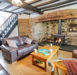 A living room with brown leather sofas a wooden coffee table with a board game and mugs a wood burning stove in a stone wall at Tai Ucha in Cerrigydrudion
