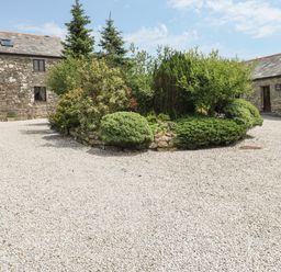 A gravel courtyard with a raised garden bed surrounded by stone buildings at The Hayloft in St Neot near Dobwalls