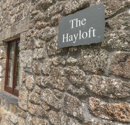 A stone exterior wall with a small window and a sign that reads The Hayloft at The Hayloft St Neot near Dobwalls
