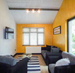 A living room with two black and gray sofas a glass coffee table a striped rug a wall-mounted television and a window with blinds at Hidden Gem Cabin in Lettermacaward near Dungloe County Donegal