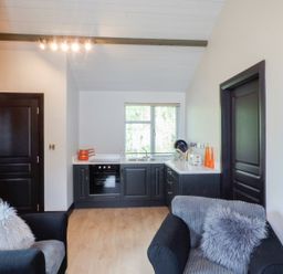 A small kitchen with black cabinets and orange pots near two black sofas with gray cushions at Hidden Gem Cabin in Lettermacaward near Dungloe County Donegal