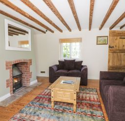 A living room with exposed wooden beams two dark sofas a wooden coffee table a brick fireplace a window and a wooden door at Blenheim Edge The Causeway in Woodstock