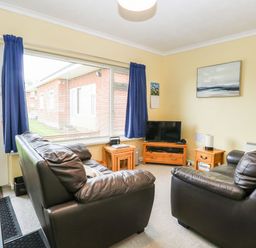 A living room with two leather sofas a TV on a wooden stand and a large window with blue curtains at 21 Siesta Mar in Mundesley