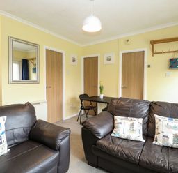 A living room with two brown leather sofas a small black table with two chairs and three wooden doors at 21 Siesta Mar in Mundesley